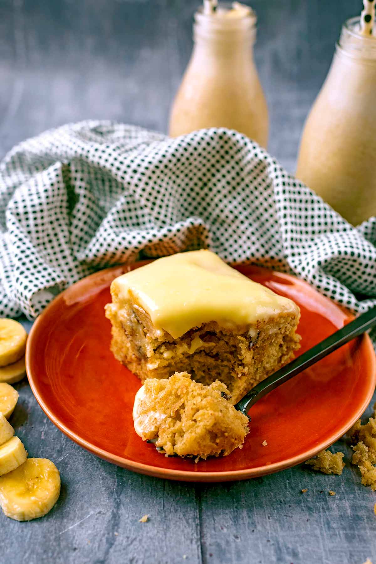 Iced Banana Cake on a red plate with a fork. Two bottles of milkshake are in the background.