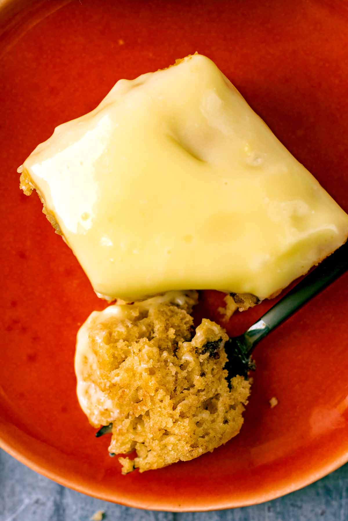 A square of iced cake with a piece cut off by a fork.