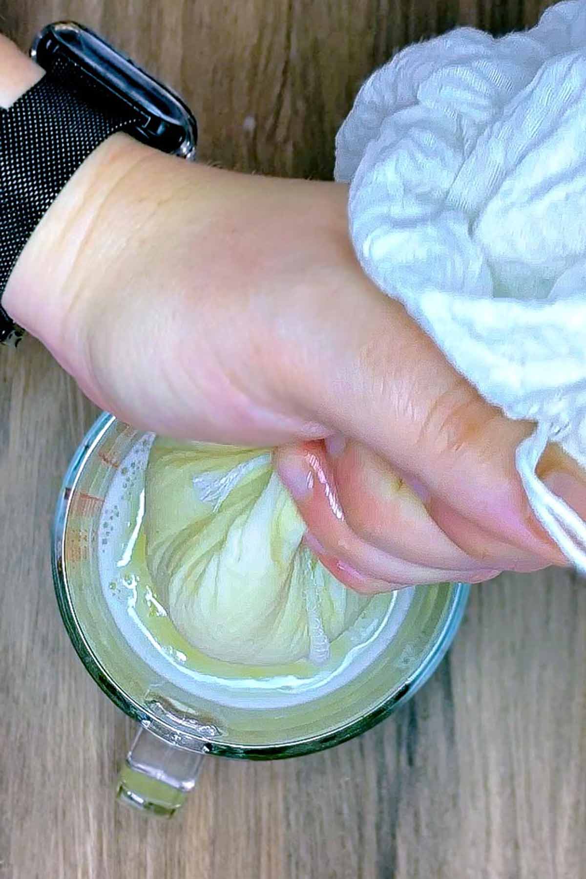 A hand squeezing juice through a nut milk bag.