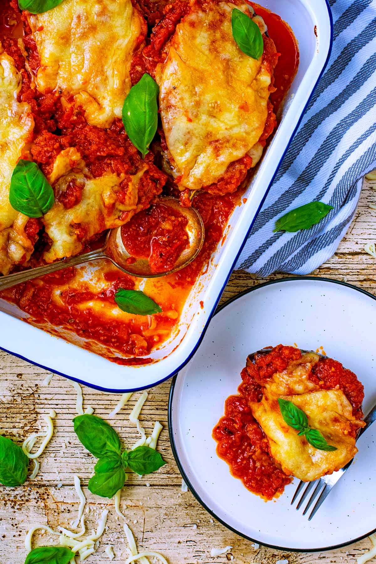 Eggplant Parmesan in a baking tray. A portion removed and put on a plate.