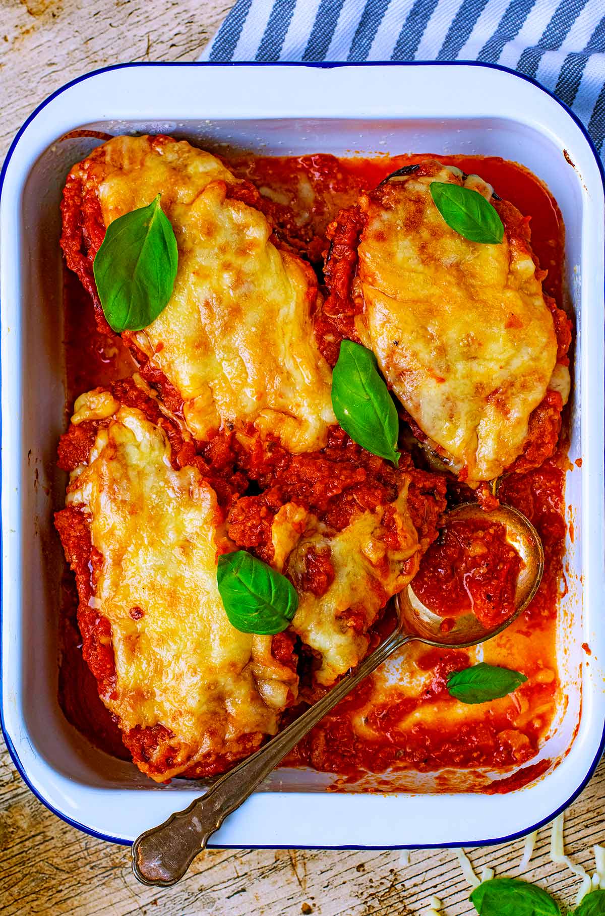 A baking tray with eggplant parmesan and a large serving spoon.