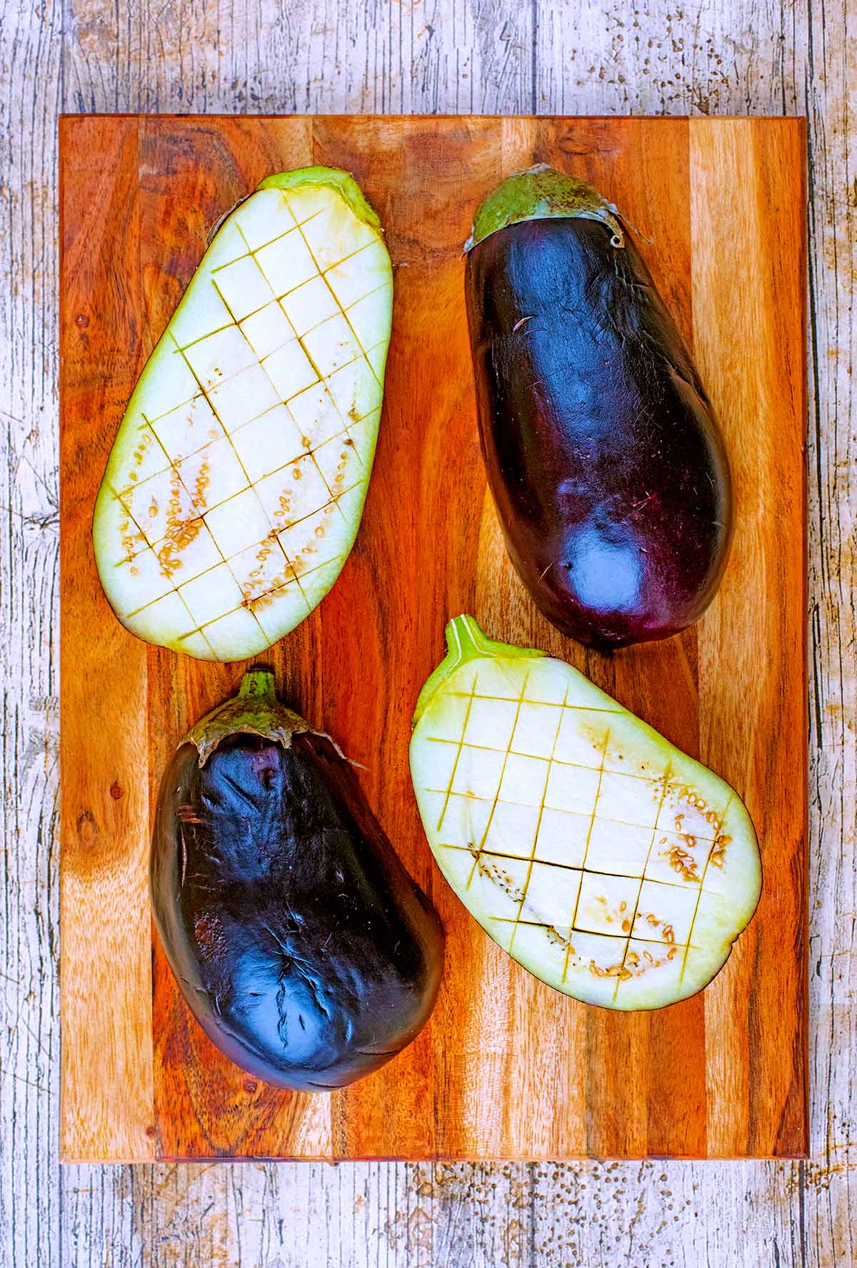 Two eggplants sliced in half and scored diagonally.