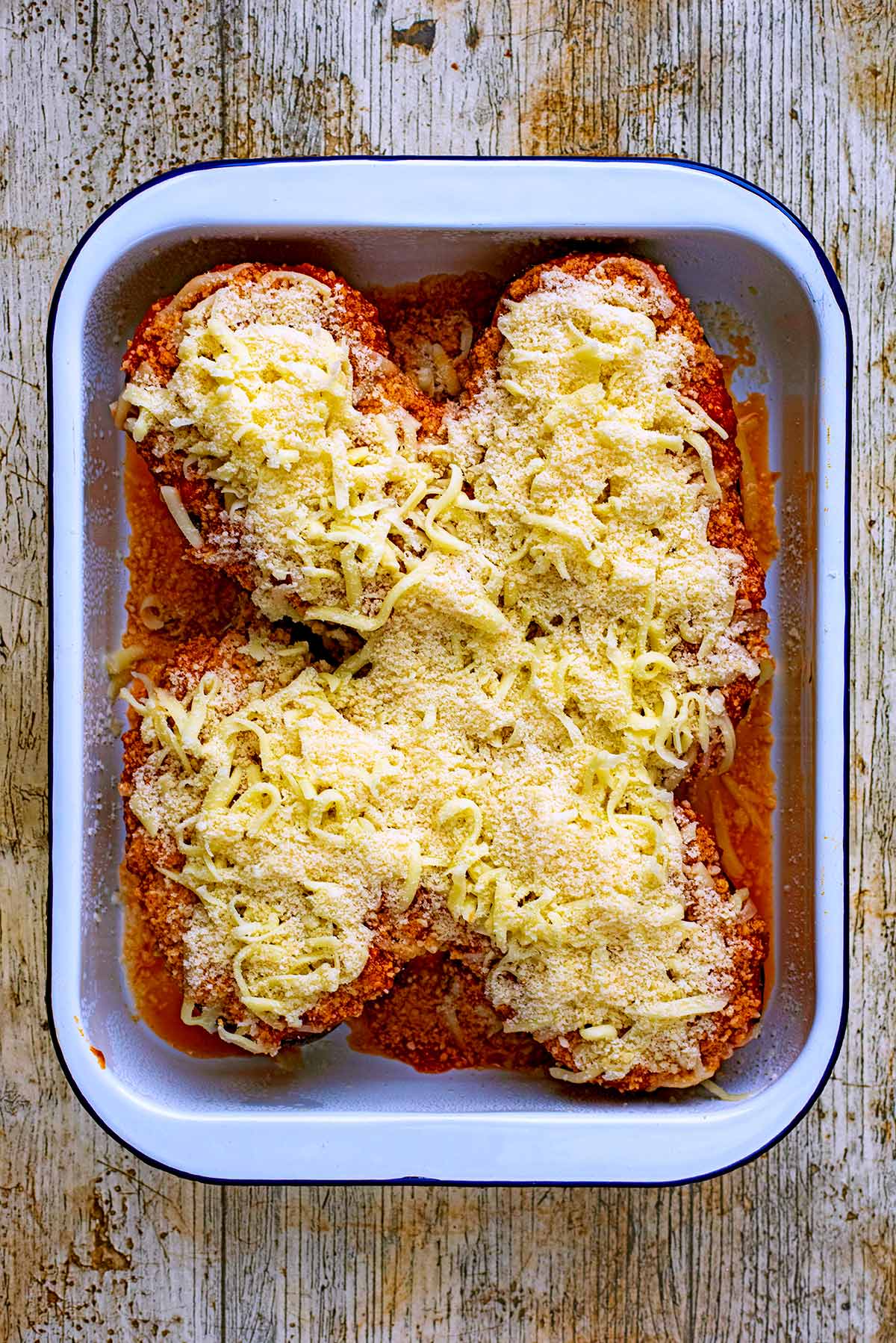 A roasting tin containing four aubergine halves covered in tomato sauce and crated cheese.