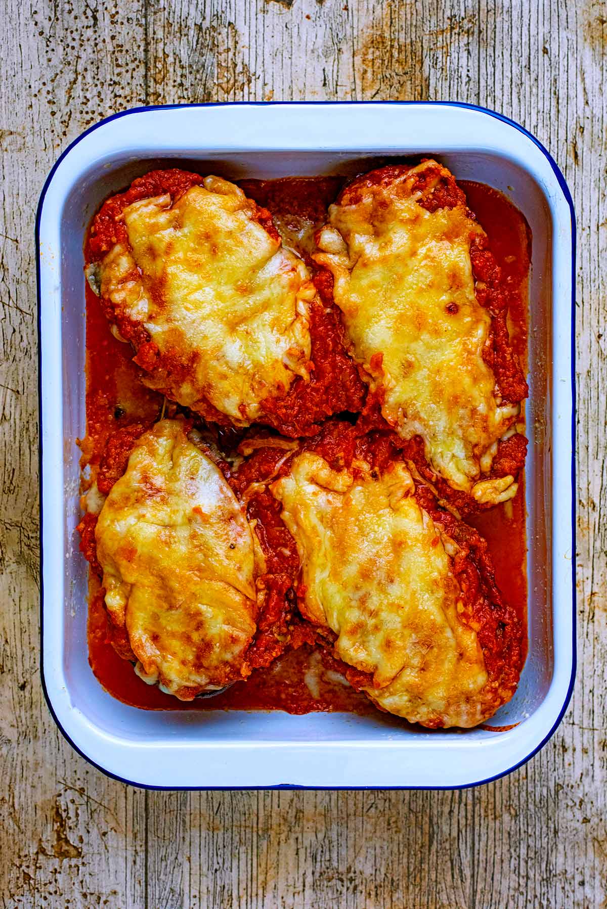 Four cooked aubergine halves covered in sauce and melted cheese.