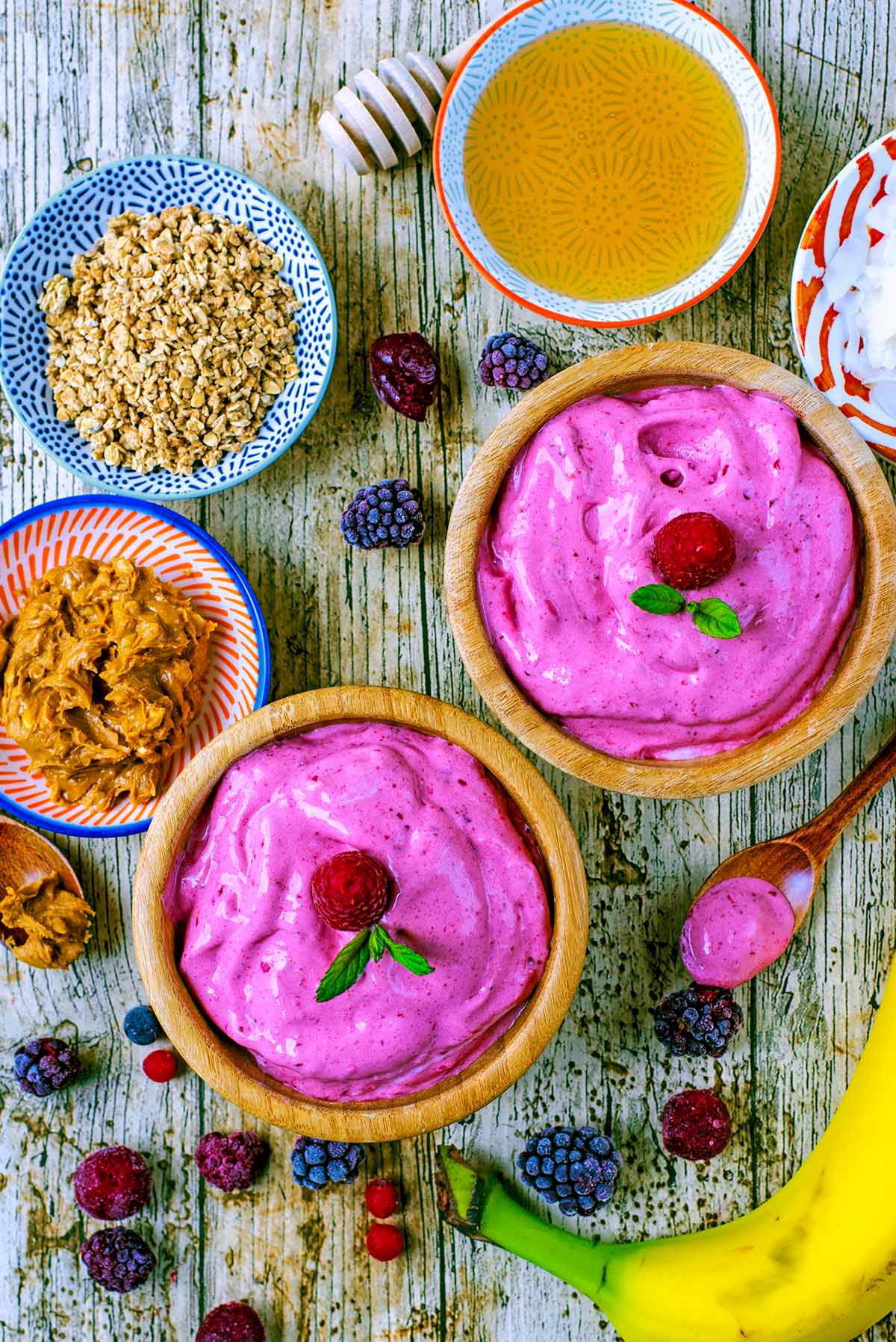 Pink Frozen Yogurt in bowls surrounded by fruit and toppings.