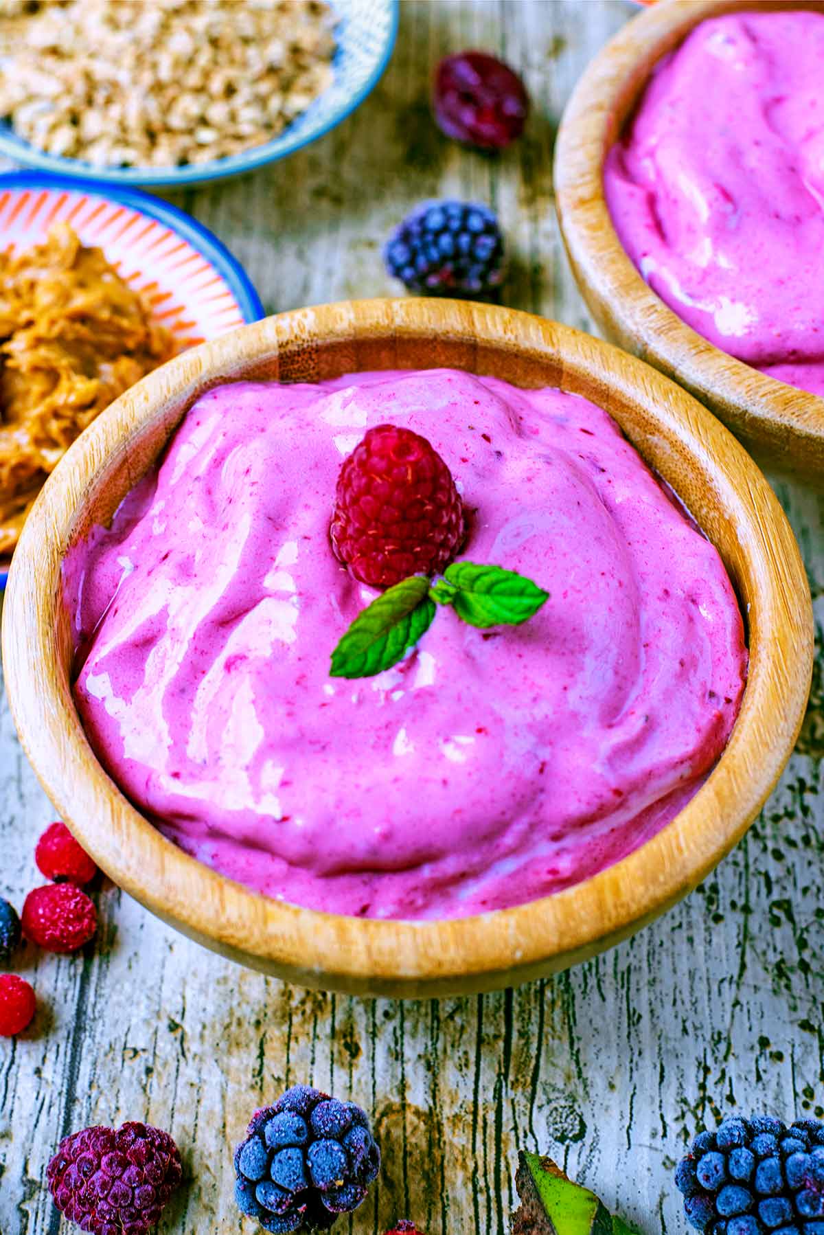 A bowl of pink frozen yogurt with a raspberry on top.