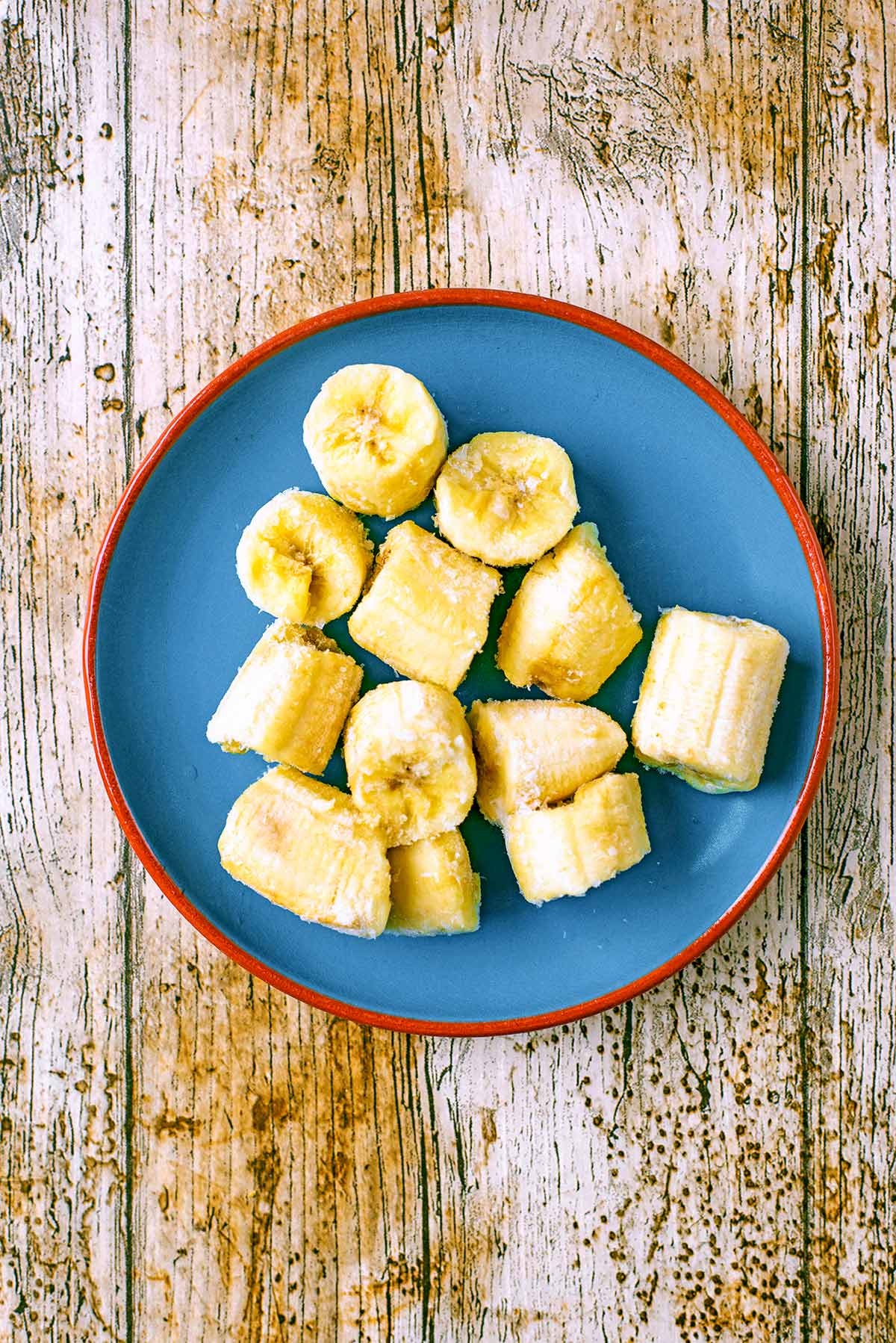 A blue plate with chunks of frozen banana on it.