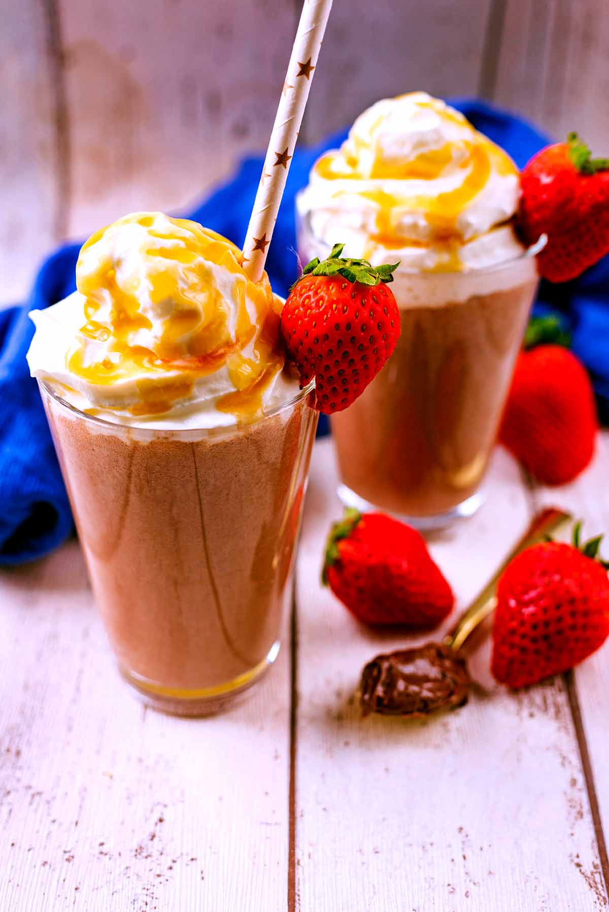 Two classes of Nutella Smoothie with whipped cream and strawberries on top.