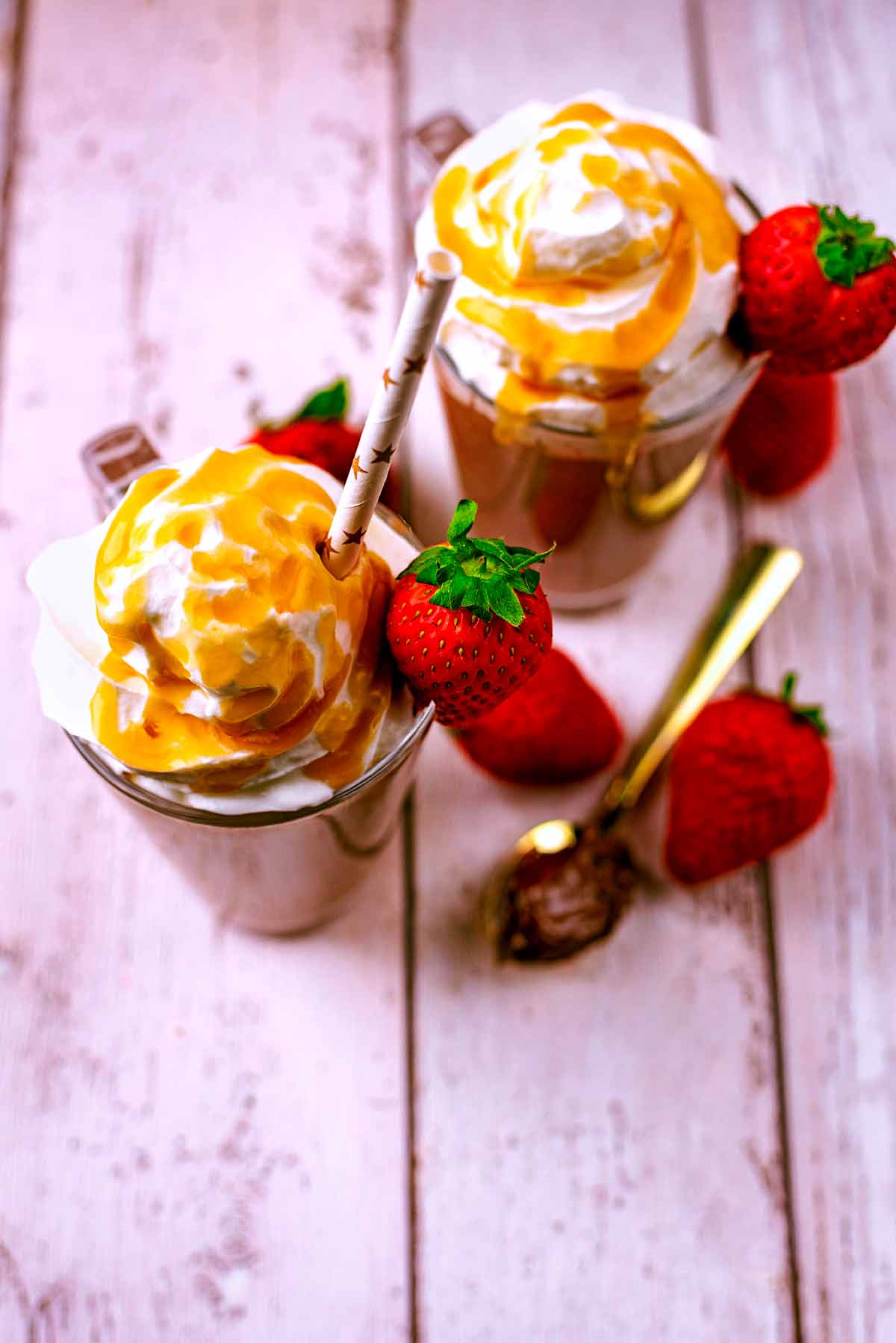 Two chocolate smoothies with cream and sauce on top. Strawberries surround the glasses.