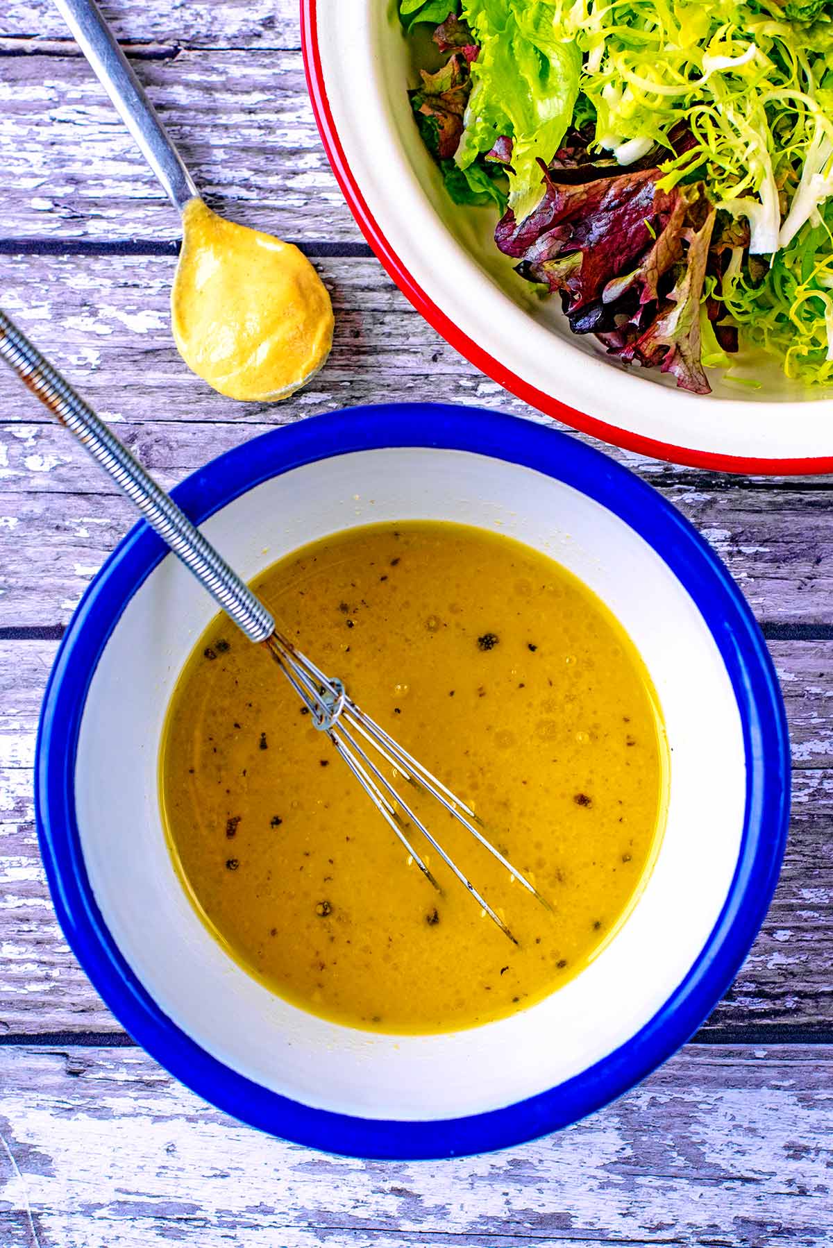 Salad dressing in a white bowl next to a bowl of salad leaves.