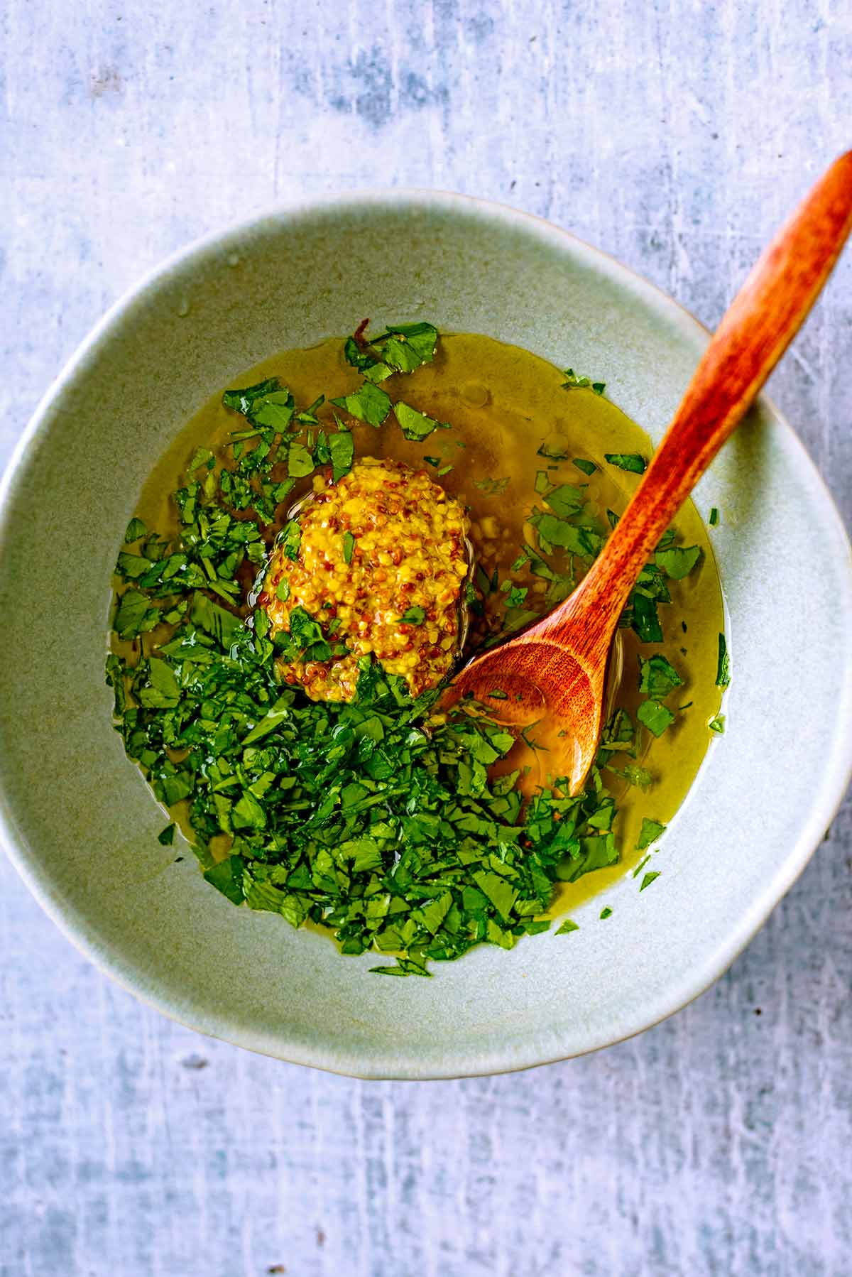 A small bowl containing, oil, honey, mustard and chopped herbs.