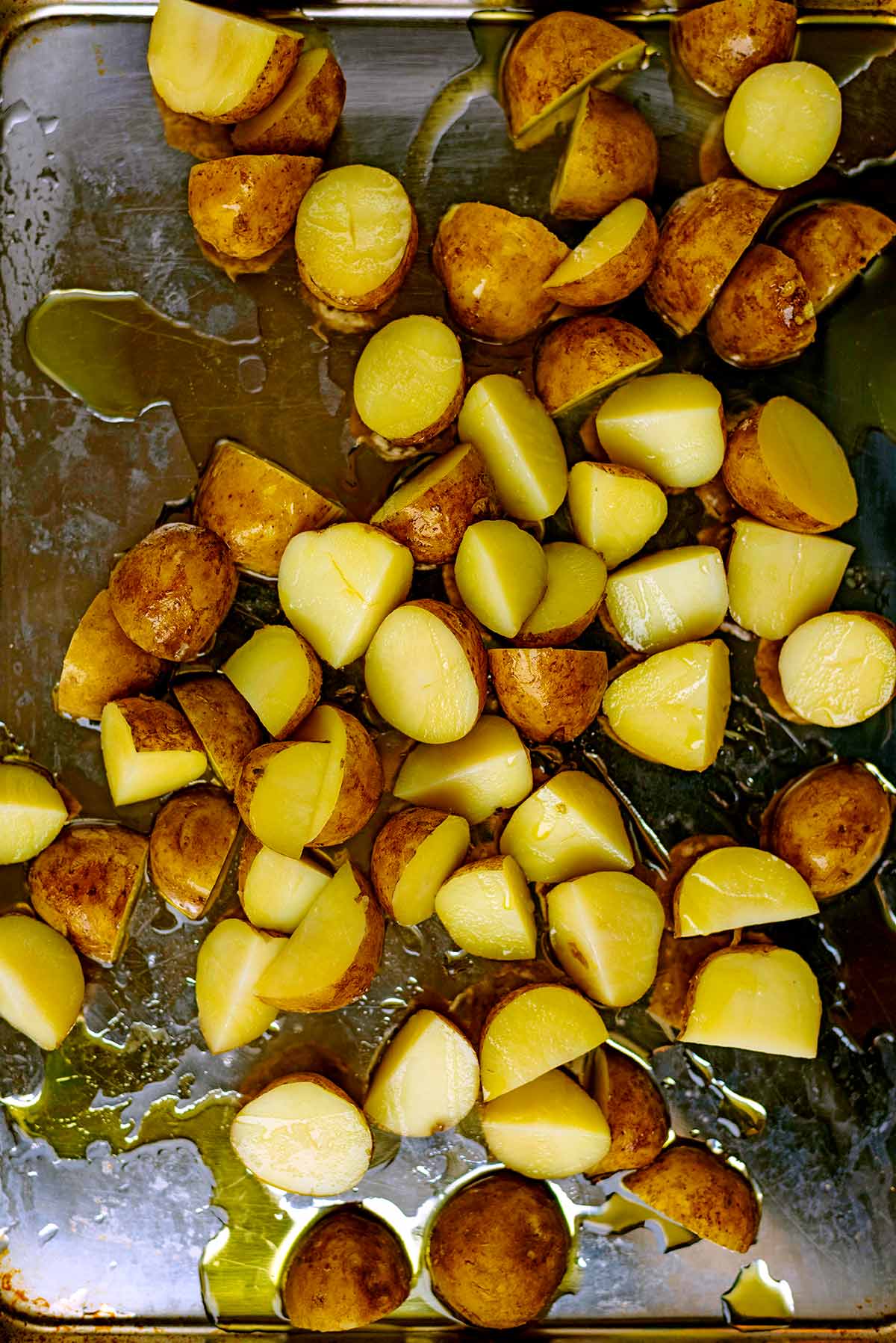A baking tray full of new potatoes cut in half covered in oil.