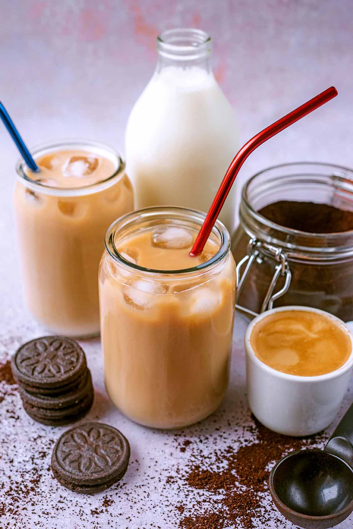Iced coffee in two glasses in front of a bottle of milk and jar of coffee grounds.