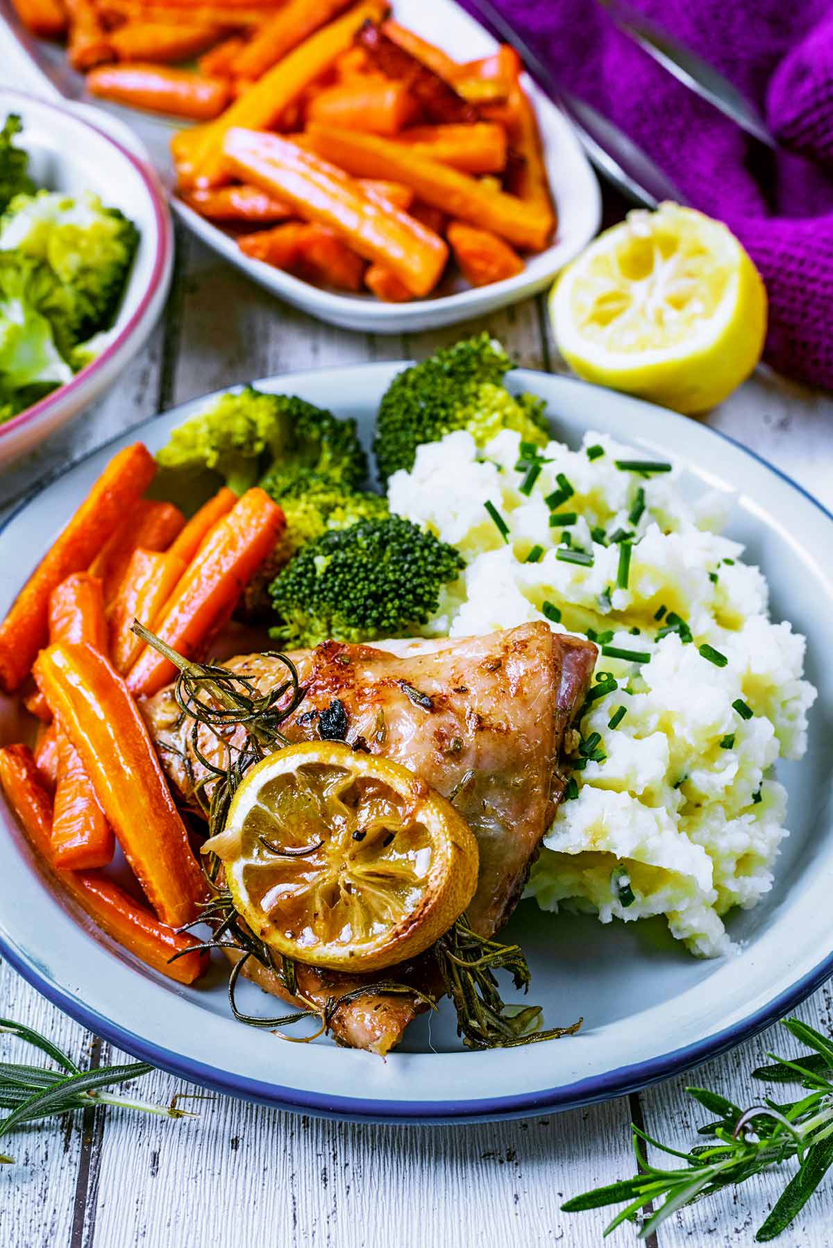 Chicken and vegetables on a white plate. A long dish of carrots is in the background.