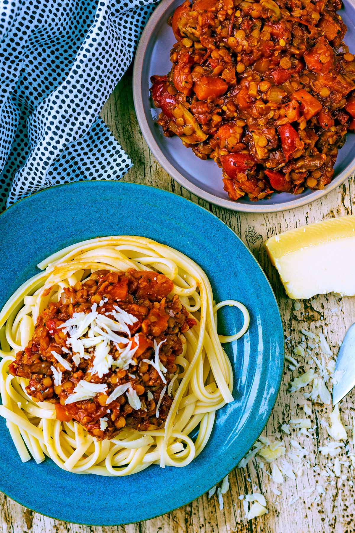 A plate of lentil bolognese and pasta topped with Parmesan shavings.