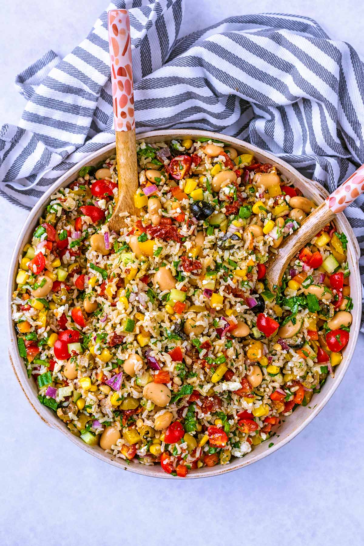 A large round dish containing Mediterranean rice salad and two wooden spoons.