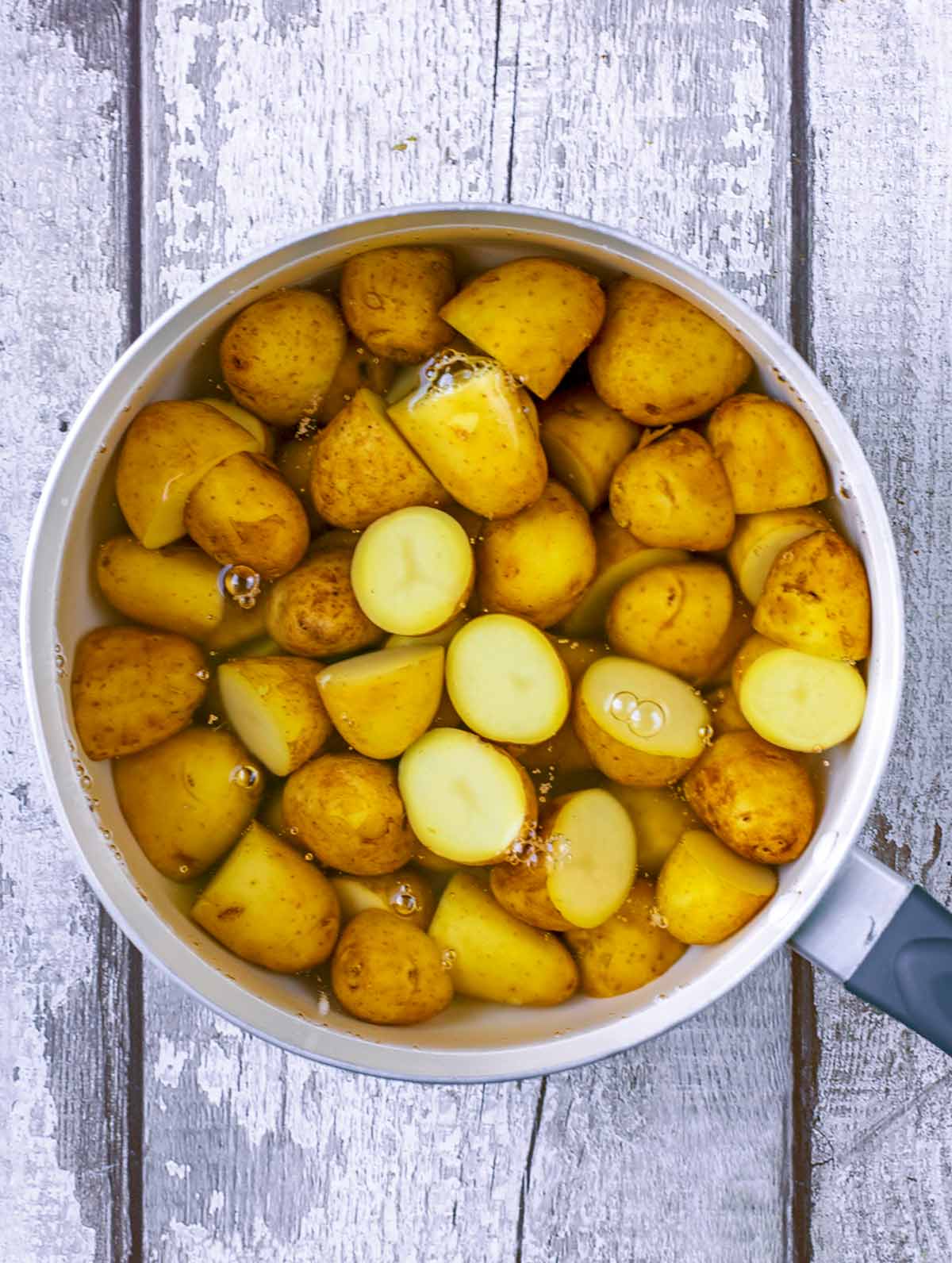 A saucepan with new potato halves in water.