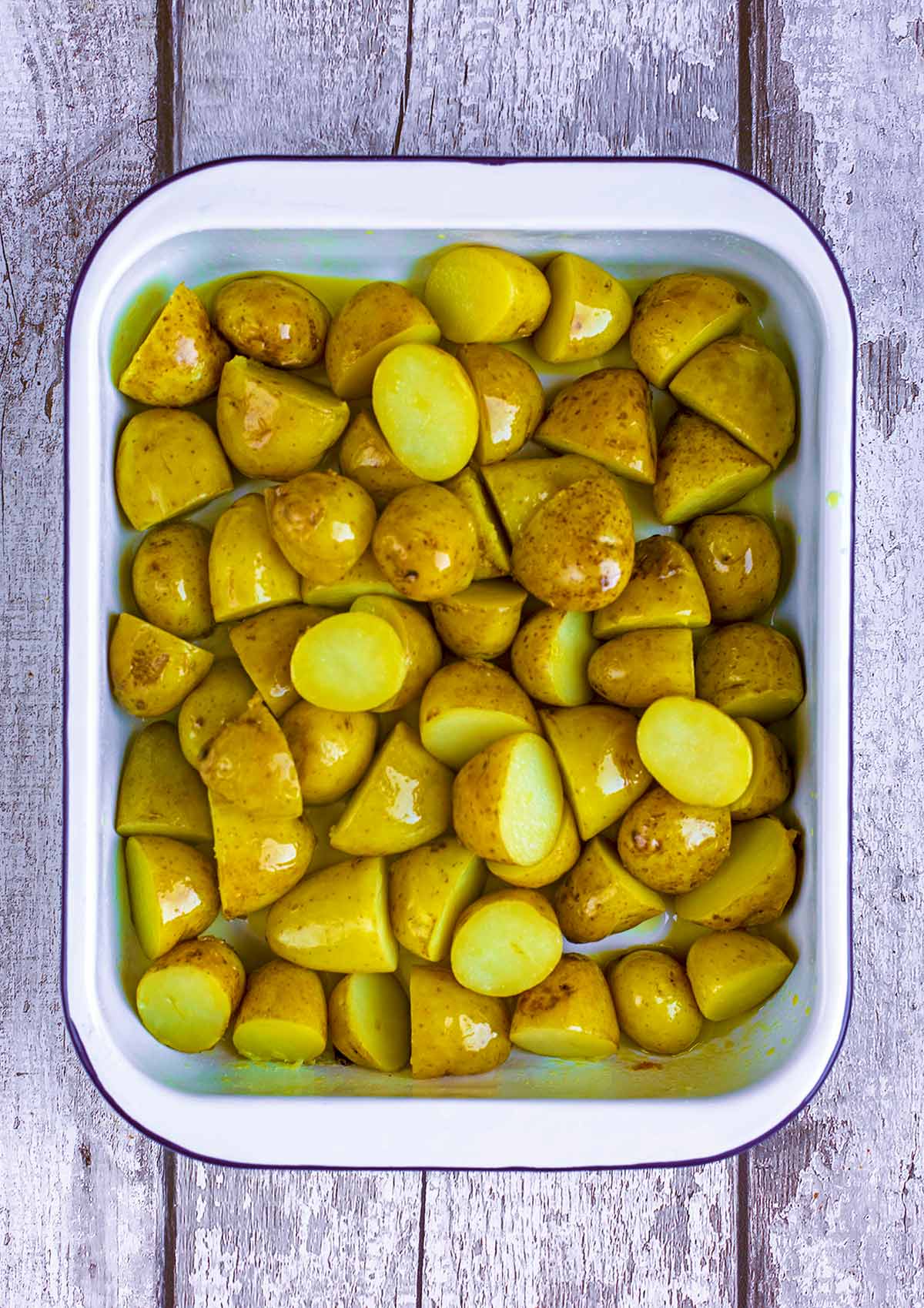 Par boiled potato halves in a baking tray with oil.