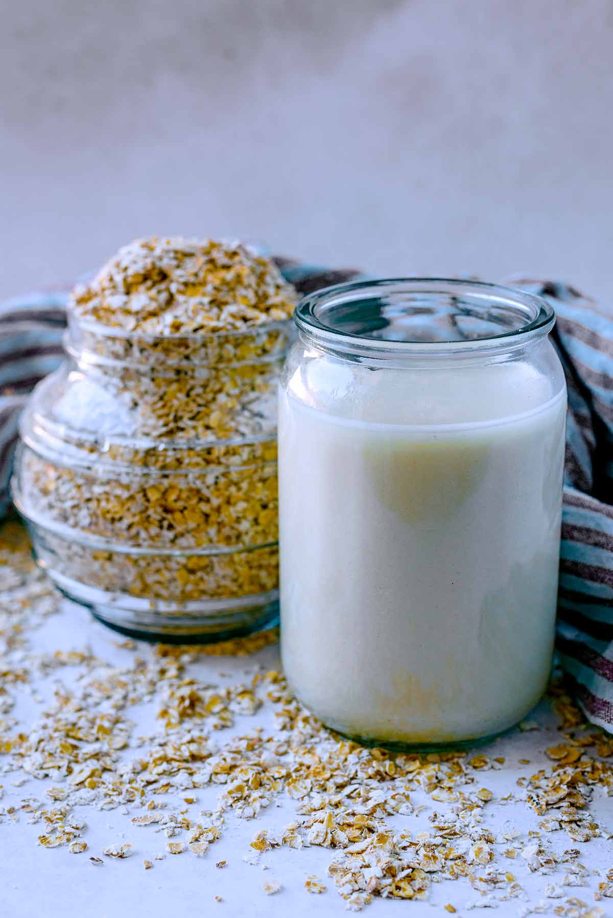 A glass of oat milk in front of a jar of oats.