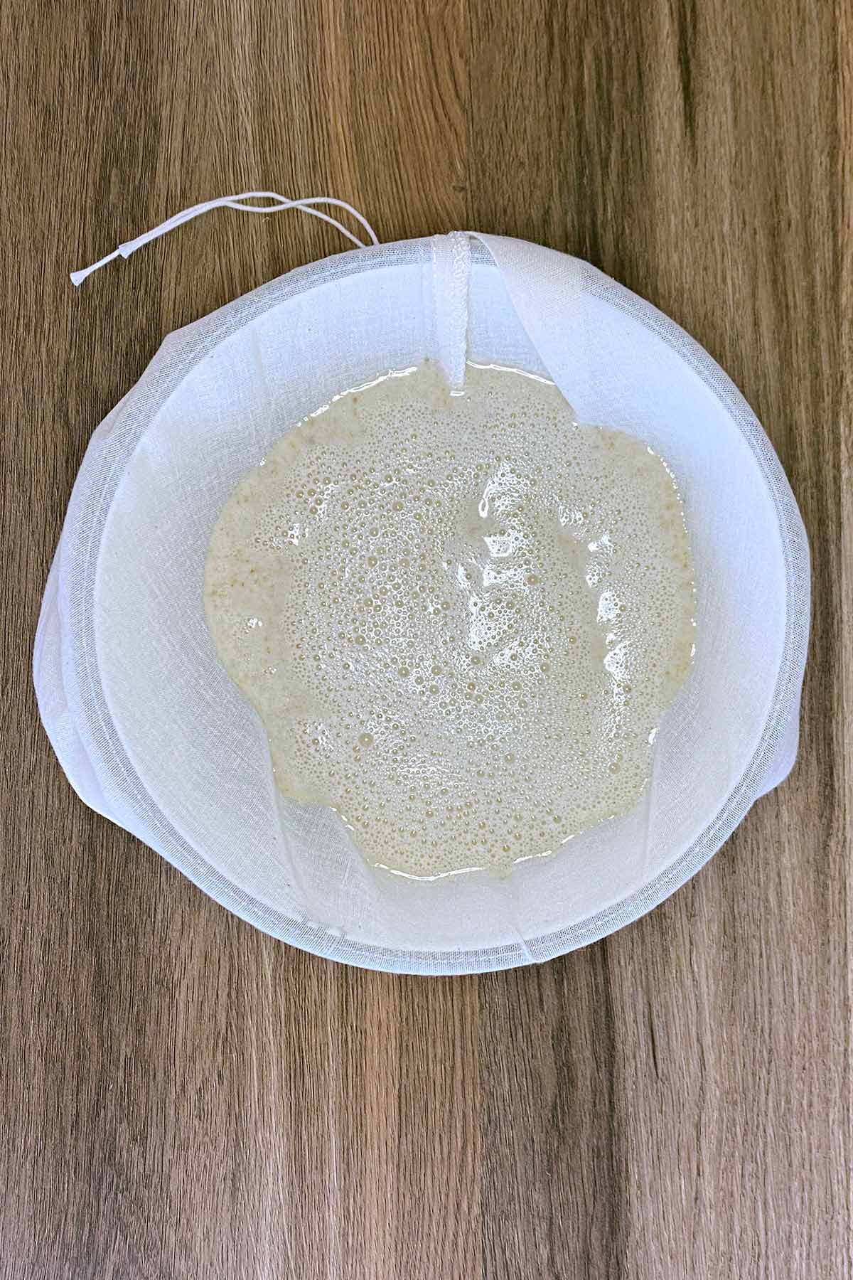 Oat milk mixture in a bag over a bowl.