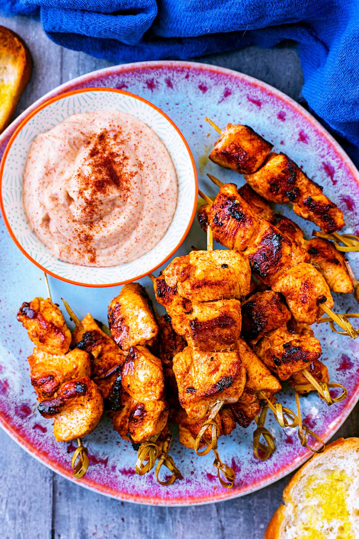 Paprika Chicken Skewers on a blue plate with a small dish of creamy dip.