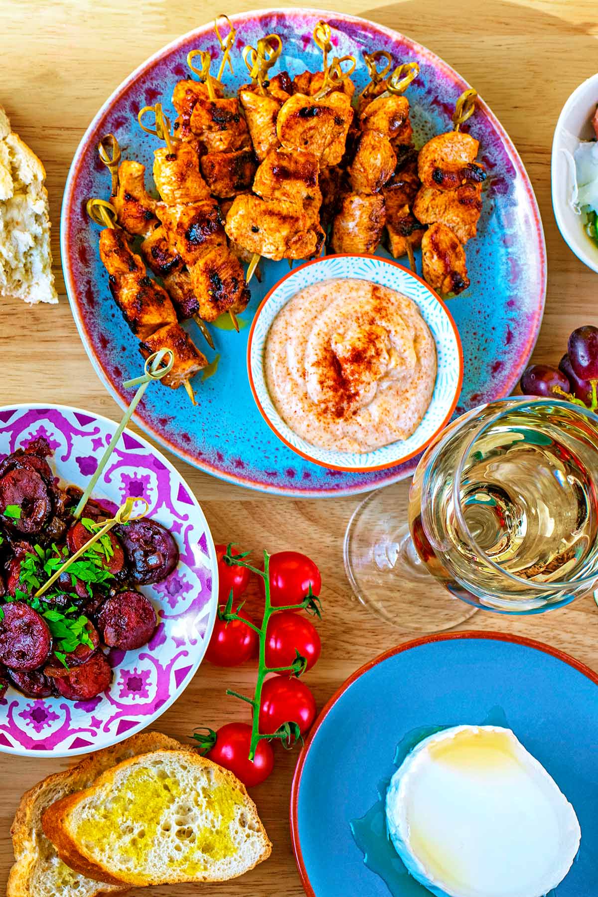 A tapas set up with chicken skewers, chorizo, goat's cheese, bread and tomatoes.