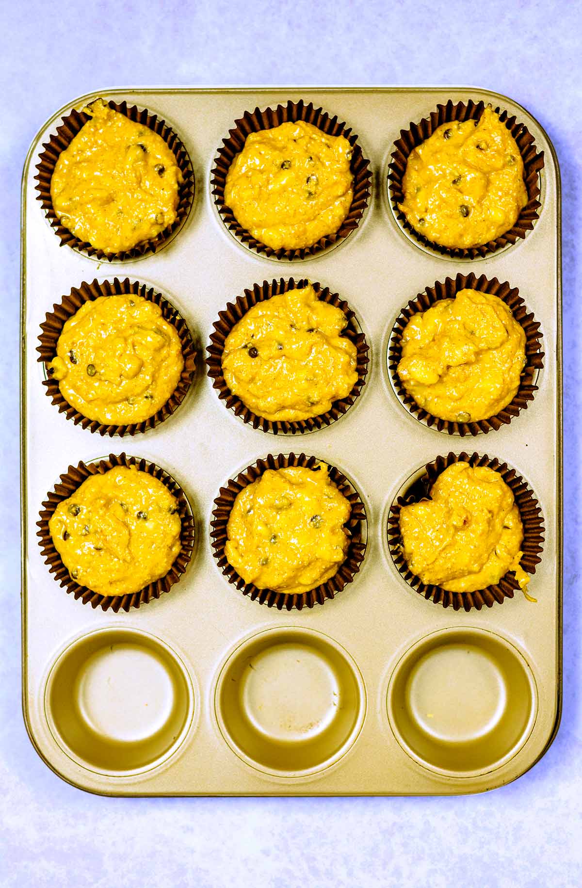 Muffin batter in nine paper cases in a muffin tin.