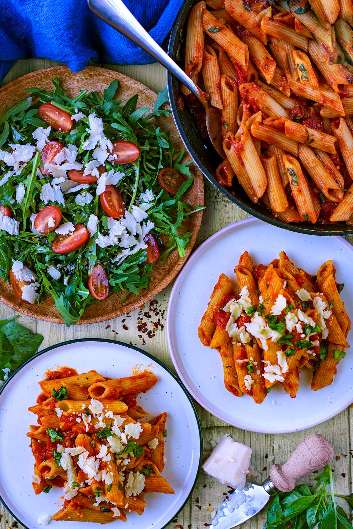 Two plates of penne arrabbiata next to a pan of more pasta and a plate of salad.