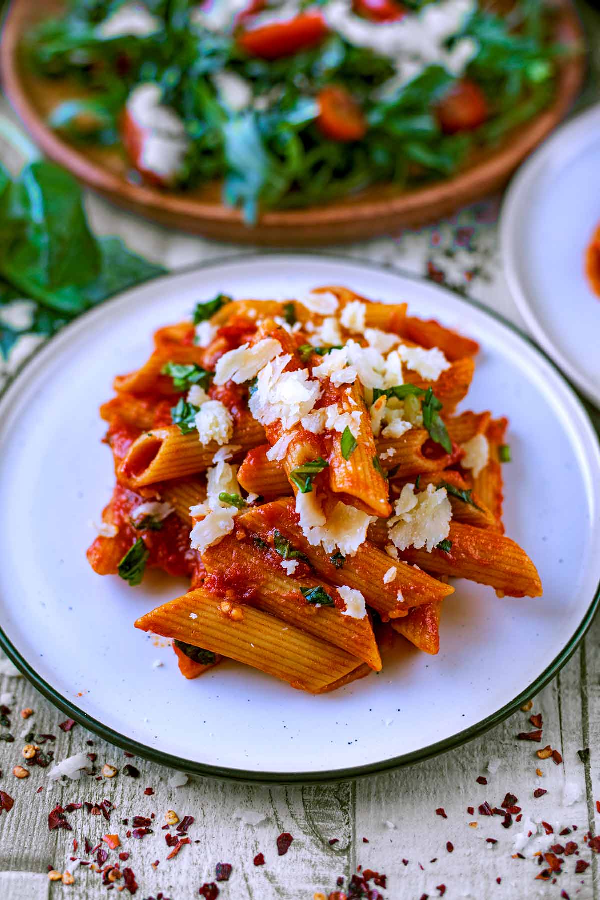 Tomato pasta on a plate in front of a plate of salad.