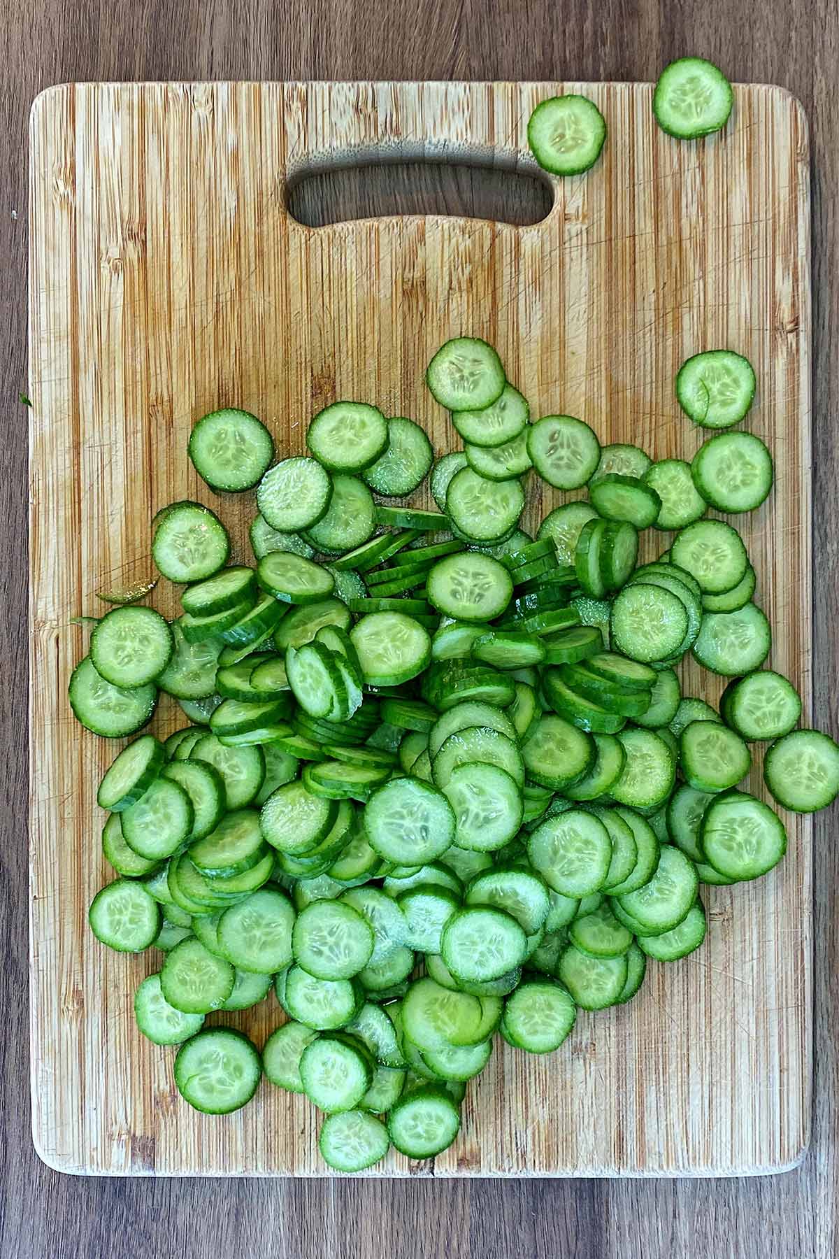 A wooden chopping board covered in slices of mini cucumbers.