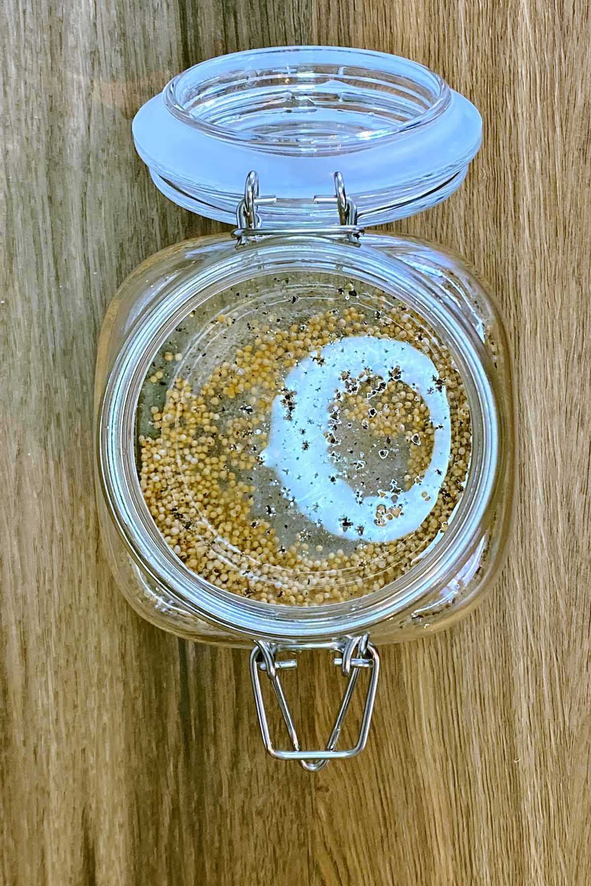 An open glass jar containing pickling vinegar and mustard seeds.