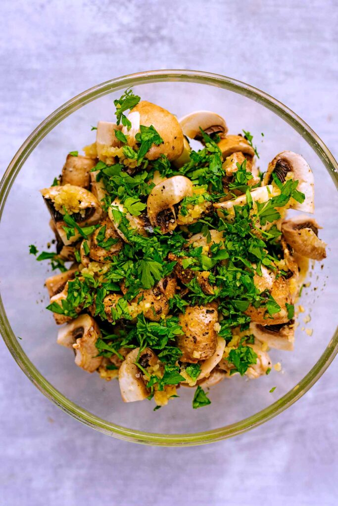 Cut mushrooms and chopped herbs in a glass bowl.