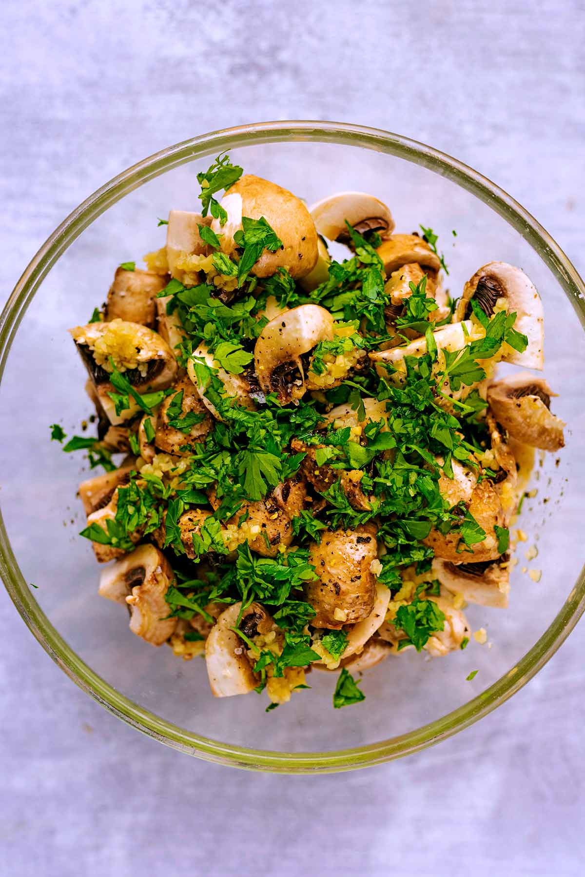A glass bowl full of quartered mushrooms and chopped herbs.