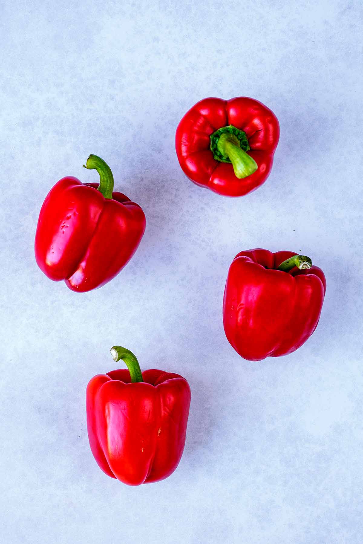 Four red bell peppers on a stone surface.