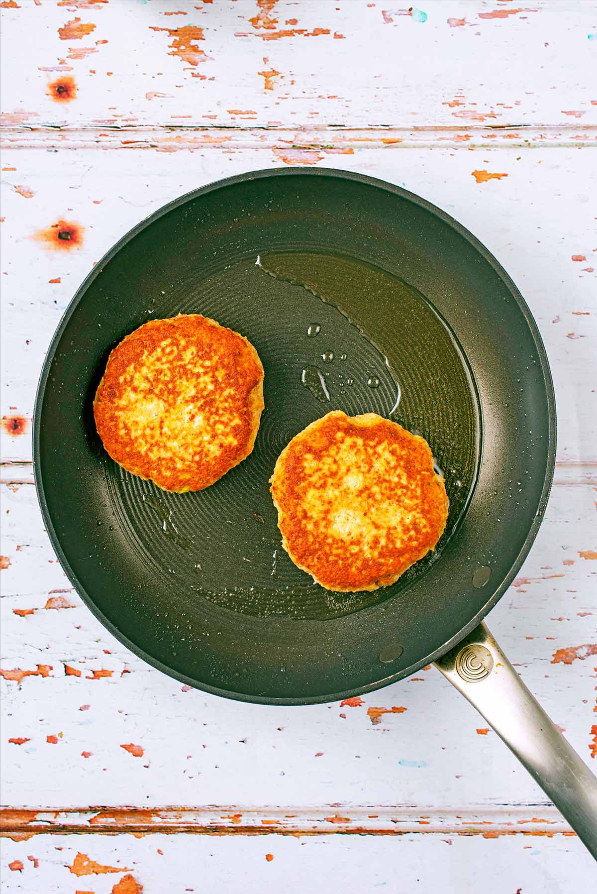Two salmon burgers frying in a pan.