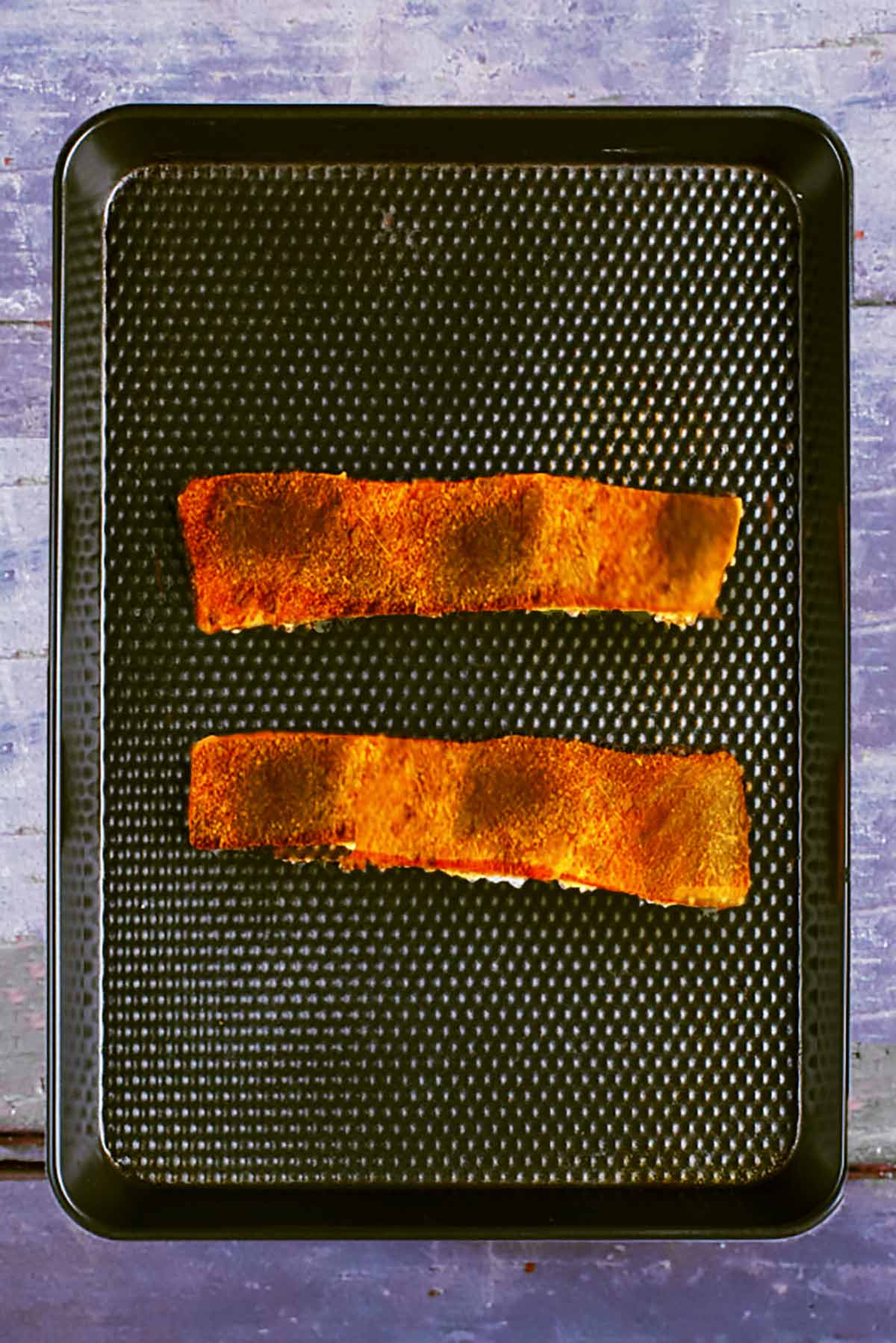 Two cooked seasoned salmon fillets on a black baking tray.