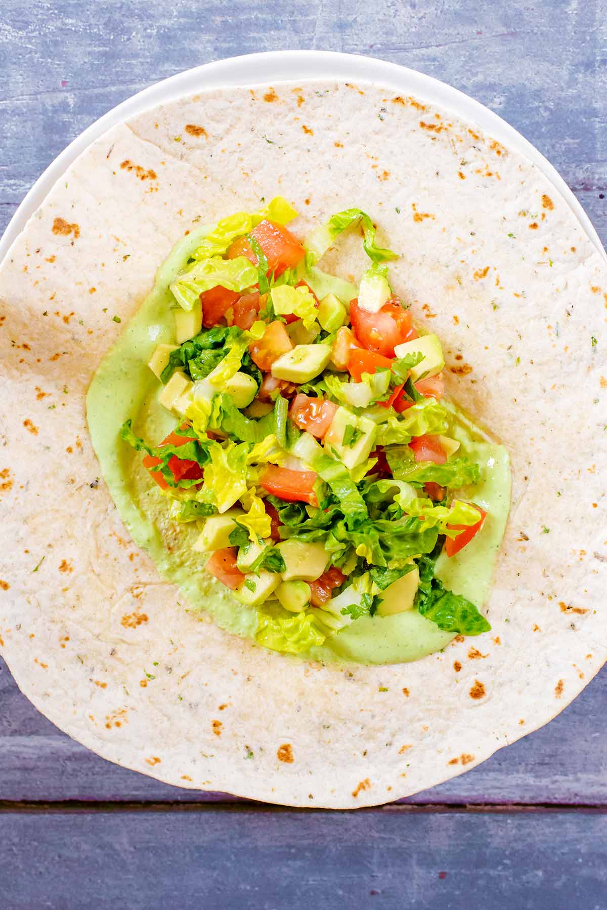 A tortilla wrap with green sauce and chopped salad.