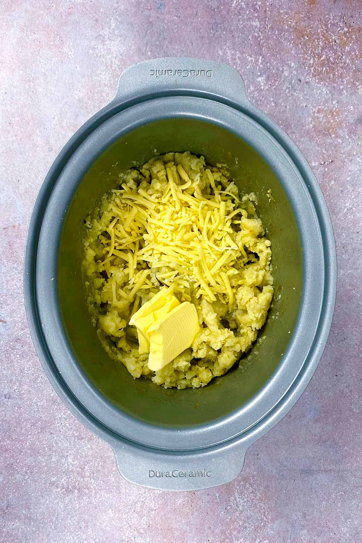 Mashed potatoes, pats of butter and grated cheese in a slow cooker.