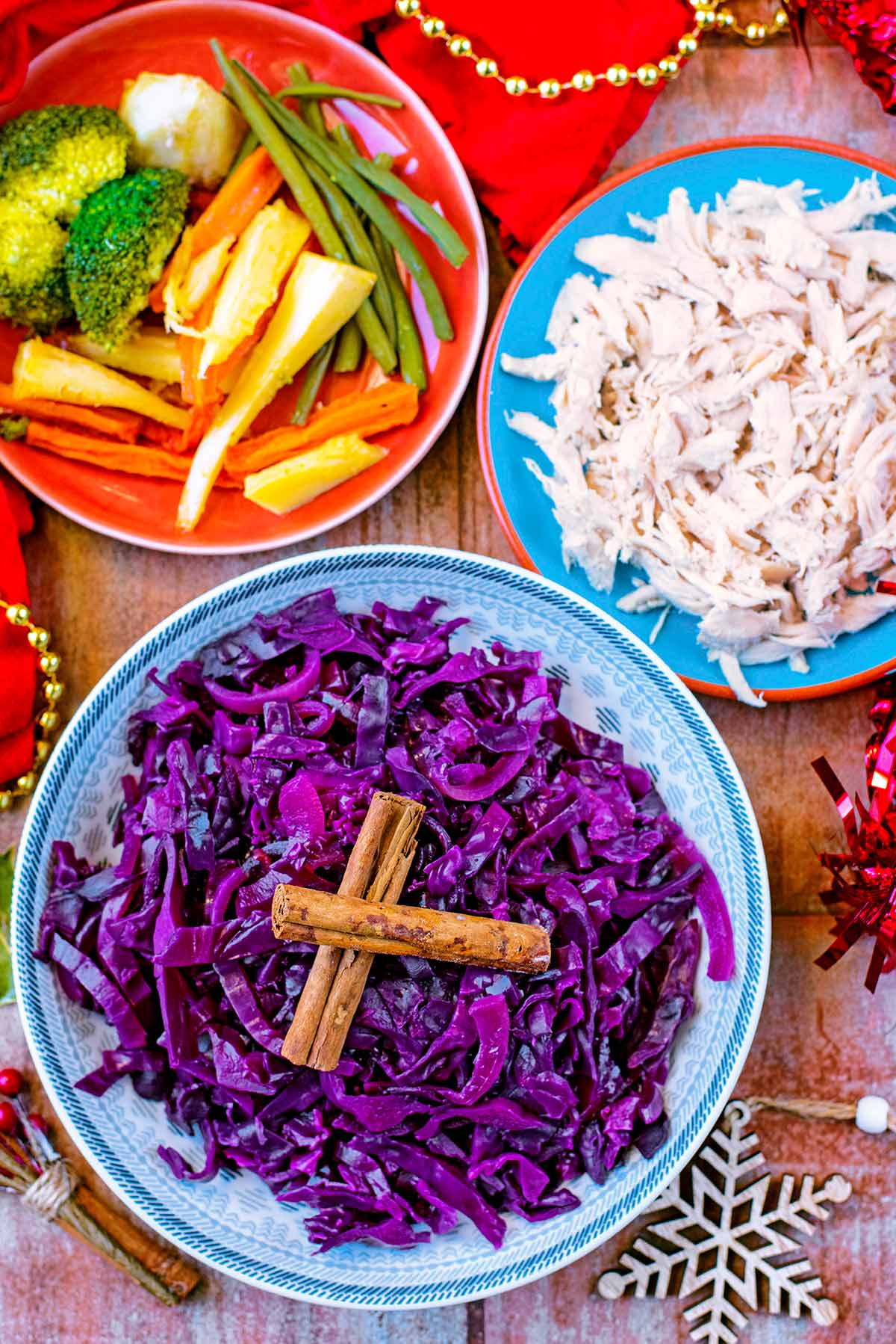 A bowl of cooked red cabbage next to some shredded turkey and some roast vegetables.