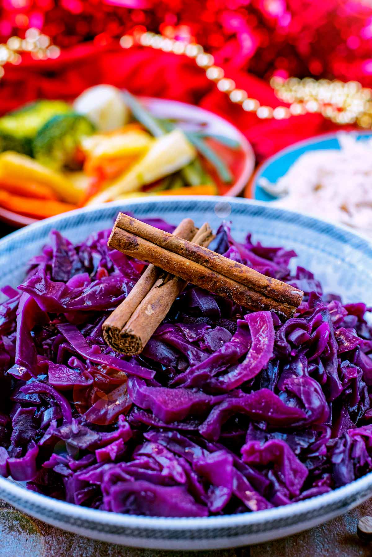 Cooked red cabbage in a large patterned bowl with cinnamon sticks on top.