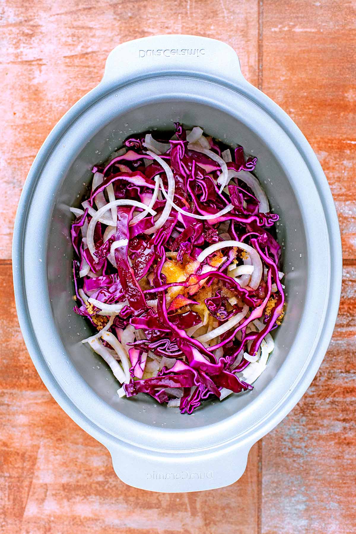 A slow cooker bowl containing shredded red cabbage and sliced onion.
