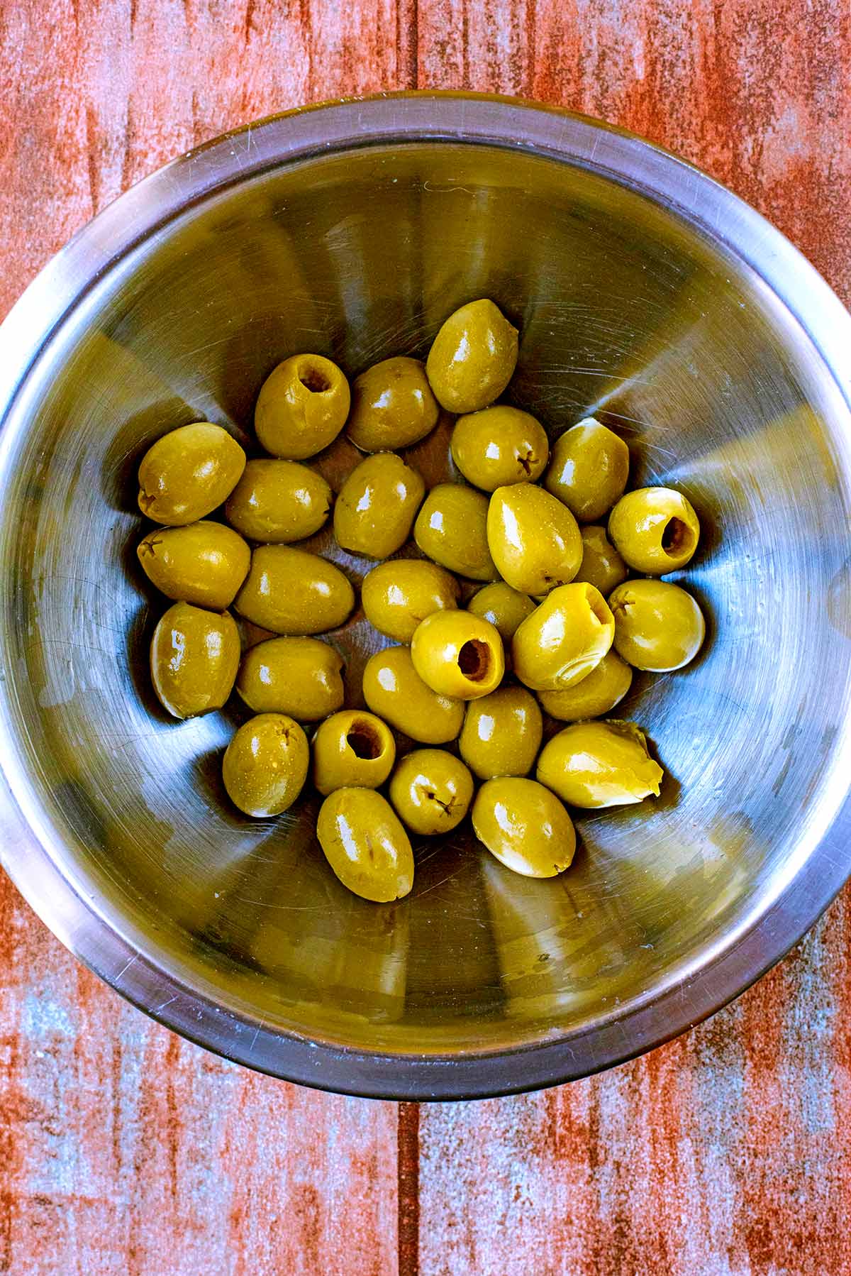 A large metal bowl containing about 30 green olives.