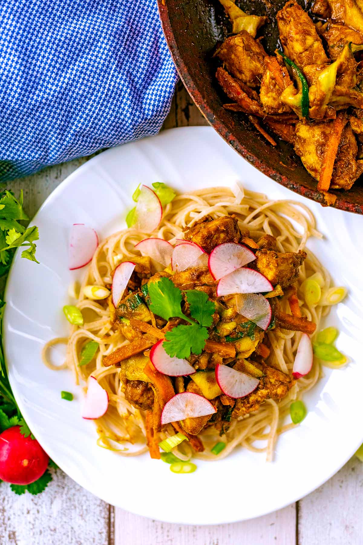 Thai Chicken Noodles on a white plate next to a pan of vegetables and chicken.