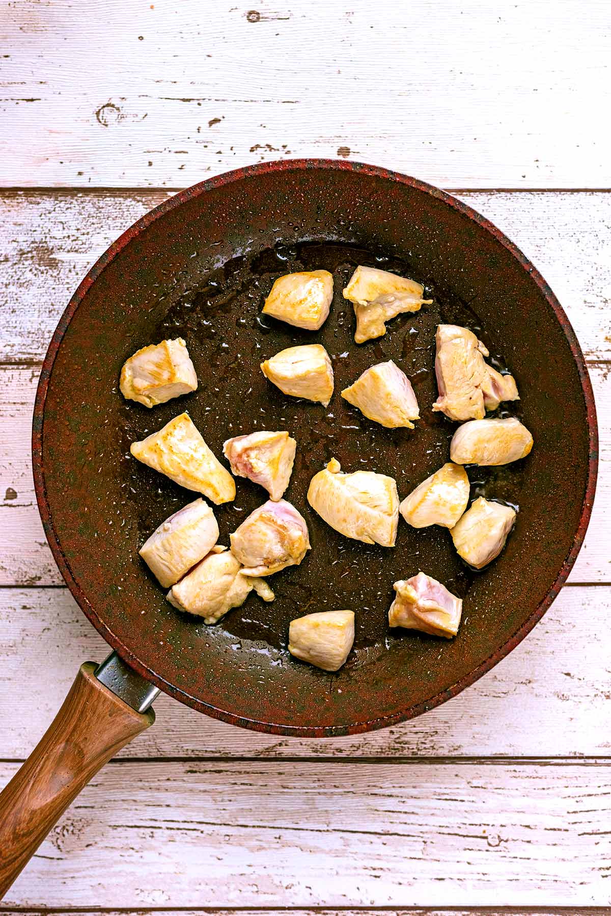 Chunks of chicken cooking in a frying pan.