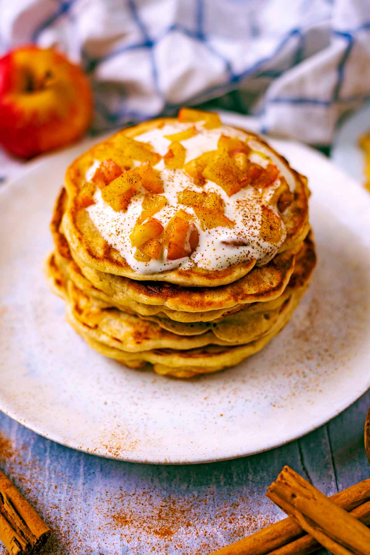 A stack of apple and cinnamon pancakes topped with yogurt and diced apple.