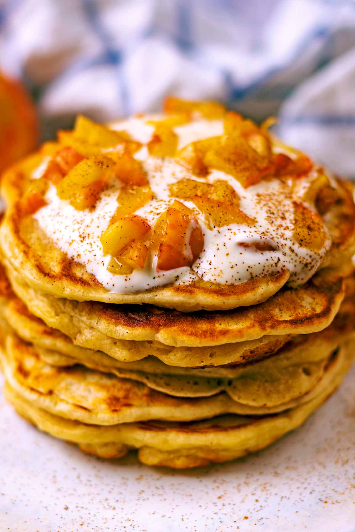 Six apple and cinnamon pancakes in a stack topped with yogurt and apples.