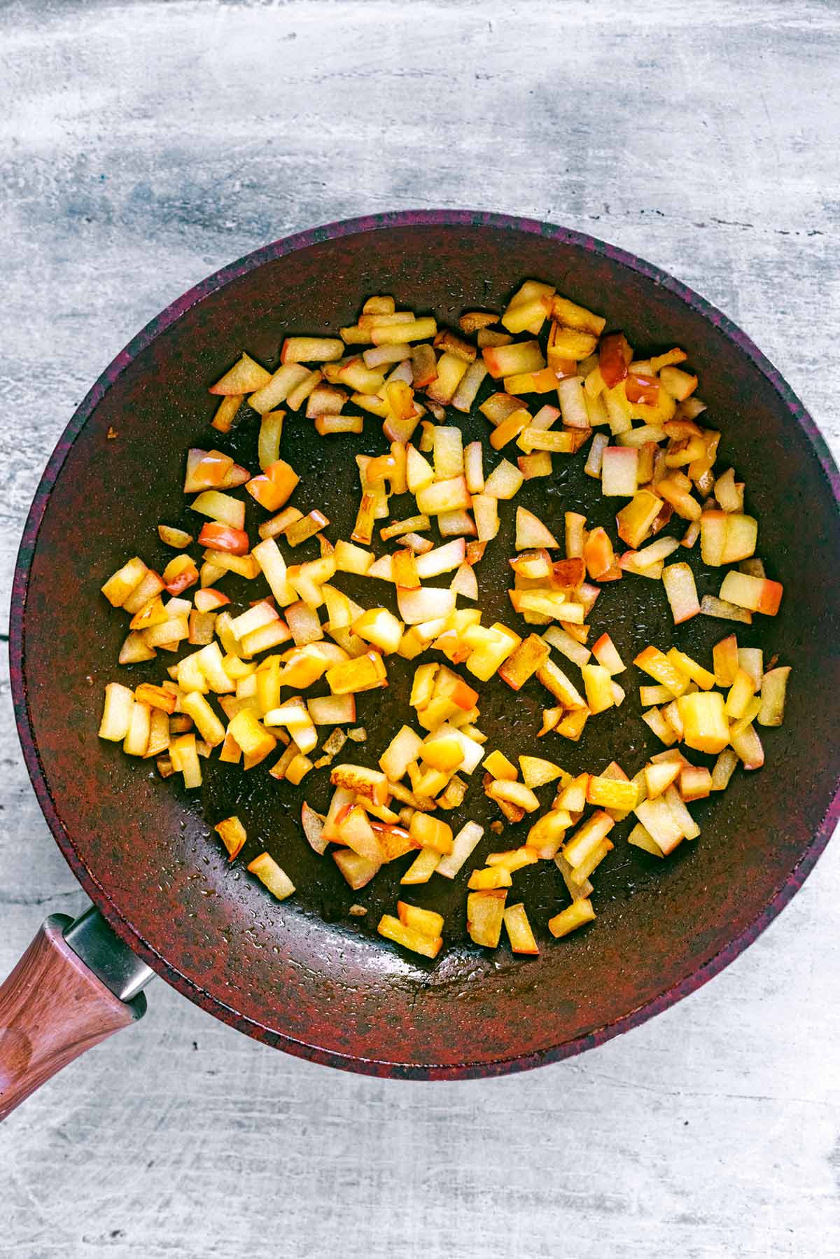 A frying pan with diced apple cooking in it.