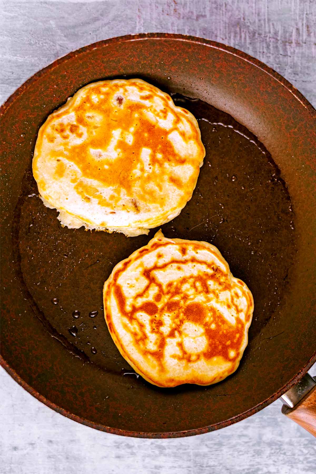 A frying pan with two pancakes being cooked in it.