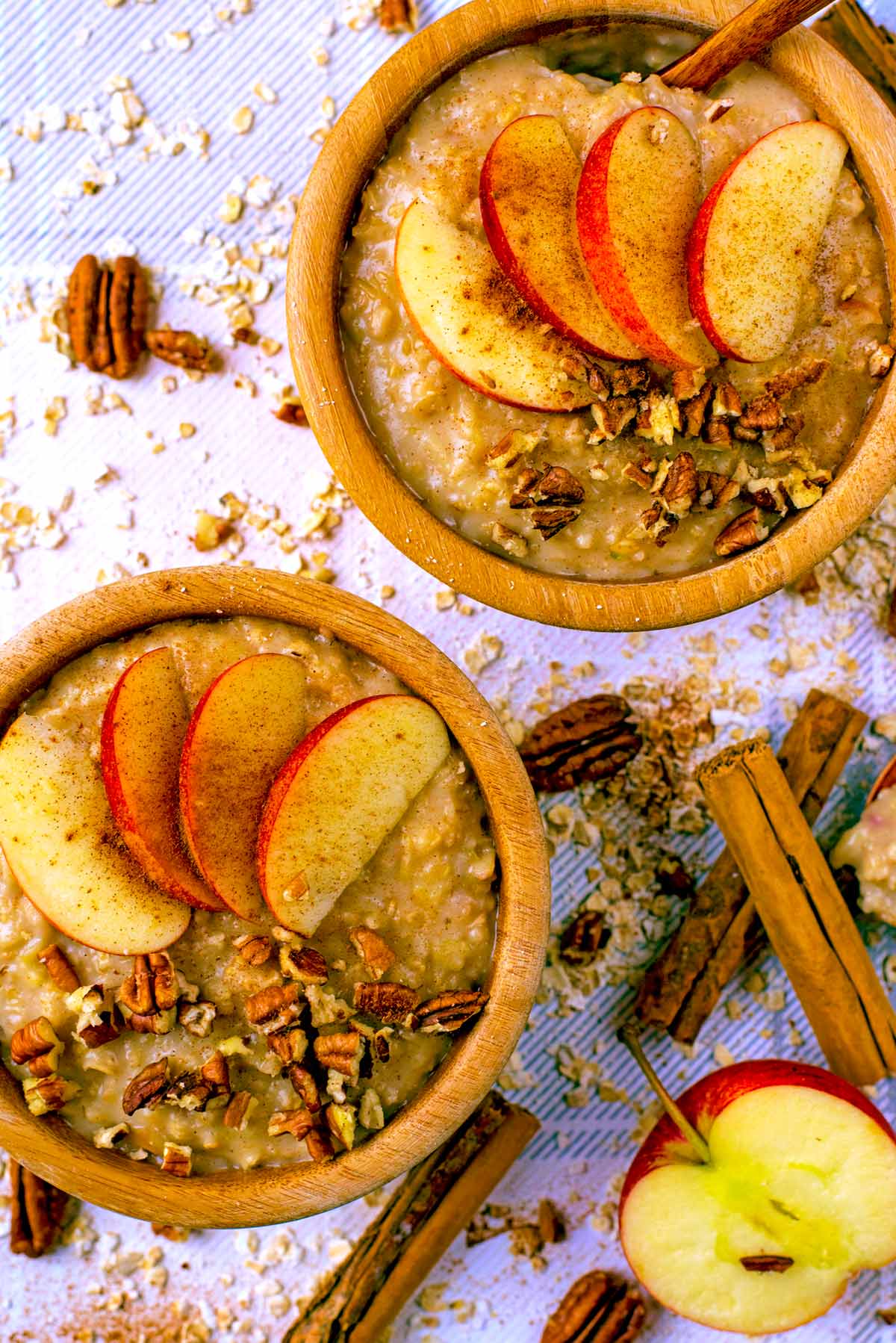 Two wooden bowls full of porridge with sliced apple on top.