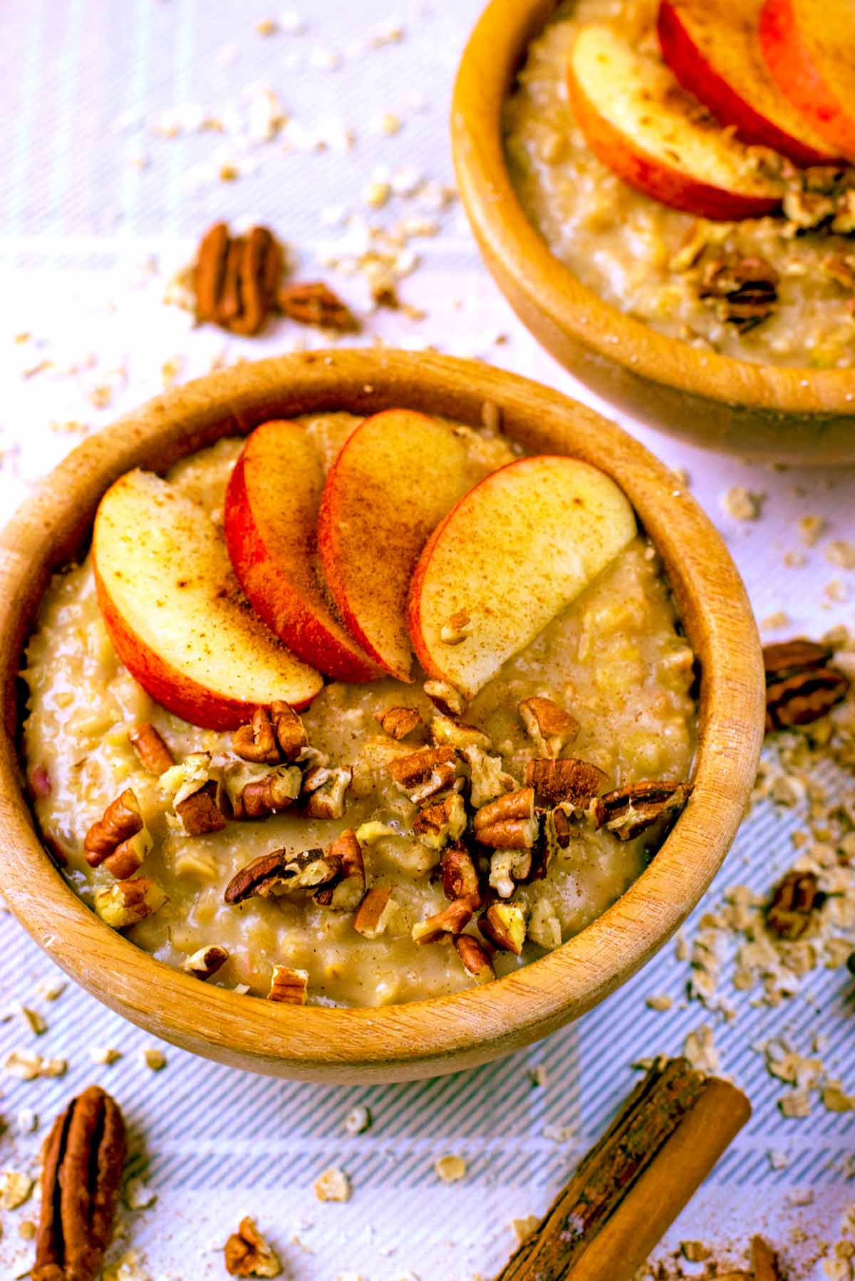 Two bowls of porridge topped with sliced apple and chopped pecans.